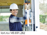 female builder holding a spirit level against window pane. Стоковое фото, агентство Ingram Publishing / Фотобанк Лори