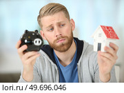 sorrowful man holding a piggybank and a model house. Стоковое фото, агентство Ingram Publishing / Фотобанк Лори