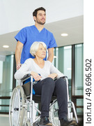 nurse pushing senior patient in wheelchair along corridor. Стоковое фото, агентство Ingram Publishing / Фотобанк Лори
