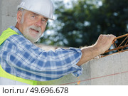 senior mason fitting rebar between layer of concrete blocks. Стоковое фото, агентство Ingram Publishing / Фотобанк Лори