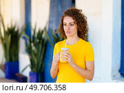 Thoughtful young curly haired female in yellow t shirt standing on street with glass jar of orange juice and looking away dreamily. Pensive woman with juice in glass jar looking away. Стоковое фото, агентство Ingram Publishing / Фотобанк Лори