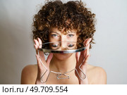 Attractive young curly haired girl model holding round mirror in hands with reflection of face and eyes while looking at camera against gray background. Girl with curly hair holding mirror in hands with reflection of eyes. Стоковое фото, агентство Ingram Publishing / Фотобанк Лори