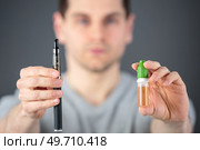 man showing an adjustable electronic cigarette and its liquid. Стоковое фото, агентство Ingram Publishing / Фотобанк Лори