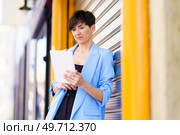 Serious entrepreneur in formal clothes standing by shining metallic gate while browsing tablet and looking at screen outdoors. Serious woman with tablet by metallic gate on street. Стоковое фото, агентство Ingram Publishing / Фотобанк Лори