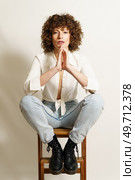 Full body of upset female model with red hair, in casual clothes resting on wooden stool with hands together and staring at camera against white background. Sad woman relaxing on ladder. Стоковое фото, агентство Ingram Publishing / Фотобанк Лори