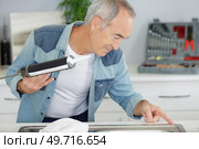 senior man using caulk gun around a sink. Стоковое фото, агентство Ingram Publishing / Фотобанк Лори