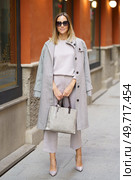 Full body of positive adult businesswoman in sunglasses and gray coat standing on pavement near shop and holding handbag. Confident stylish female standing on sidewalk. Стоковое фото, агентство Ingram Publishing / Фотобанк Лори