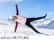 Full body of positive young female in cozy clothes and stylish sunglasses, stretching arms in side plank yoga pose with open legs on snowy ground against blue sky. Happy woman with eyeglasses in side plank yoga handstand pose. Стоковое фото, агентство Ingram Publishing / Фотобанк Лори