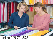 two smiling women selecting textiles in fabric store. Стоковое фото, агентство Ingram Publishing / Фотобанк Лори