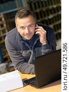 portrait of smiling storeman with laptop and using cellphone. Стоковое фото, агентство Ingram Publishing / Фотобанк Лори