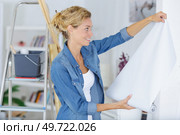 woman unrolling a wall paper on the wall. Стоковое фото, агентство Ingram Publishing / Фотобанк Лори