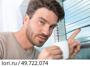 man holding cup and peeking through window blinds. Стоковое фото, агентство Ingram Publishing / Фотобанк Лори