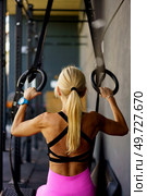Back view of muscular young fit female with ponytail in activewear exercise on gymnastic rings during fitness training at modern sport club against blurred background. Unrecognizable fit lady exercising with gymnastic rings in fitness center. Стоковое фото, агентство Ingram Publishing / Фотобанк Лори