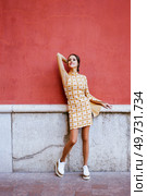Full body of young sensual female model in makeup with stylish dress and trendy footwear standing on street raising elbow while looking at camera. Young woman standing on street by wall. Стоковое фото, агентство Ingram Publishing / Фотобанк Лори