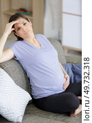 pregnant woman has stomachache sitting on her couch. Стоковое фото, агентство Ingram Publishing / Фотобанк Лори