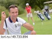 Portrait of male golfer, wife playing in background. Стоковое фото, агентство Ingram Publishing / Фотобанк Лори