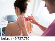 Crop professional osteopath applying kinesiology tape on neck of unrecognizable young female patient in inner wear during physiotherapy session in clinic. Woman applying soothing kinesiology tape on neck of client. Стоковое фото, агентство Ingram Publishing / Фотобанк Лори