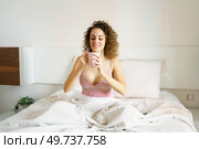 Happy young woman in sleepwear looking at coffee cup while sitting in bed during morning at home. Happy woman in sleepwear looking at coffee cup while sitting in bed. Стоковое фото, агентство Ingram Publishing / Фотобанк Лори