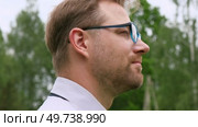 Confident Businessman in Natural Setting. Man stands in front of lush green backdrop. Remote working. Portrait of happy mid adult male wearing formal clothes, shirt and tie, glasses. Find inspiration. Стоковое видео, видеограф Марина Демидюк / Фотобанк Лори