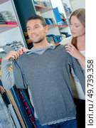 Couple in clothes shop, lady holding jumper against man. Стоковое фото, агентство Ingram Publishing / Фотобанк Лори