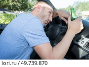 man holding bottle of beer slumped over car steering wheel. Стоковое фото, агентство Ingram Publishing / Фотобанк Лори