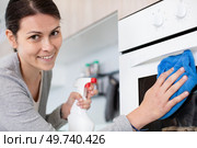 happy woman with bottle of spray cleanser cleaning domestic oven. Стоковое фото, агентство Ingram Publishing / Фотобанк Лори