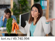 woman holding bunch of carrots in an office. Стоковое фото, агентство Ingram Publishing / Фотобанк Лори