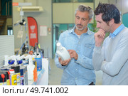 Two men looking at label of mechanical product. Стоковое фото, агентство Ingram Publishing / Фотобанк Лори