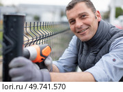 man cordless-drill erecting a wire fence. Стоковое фото, агентство Ingram Publishing / Фотобанк Лори