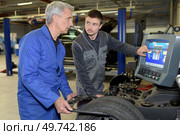 apprentice mechanic and teacher retreading wheel in automotive workshop. Стоковое фото, агентство Ingram Publishing / Фотобанк Лори