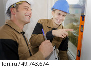 two builders holding spirit level against window and laughing. Стоковое фото, агентство Ingram Publishing / Фотобанк Лори