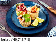 Puff pastry tartlets or canapes with fish, shrimp and bacon on a plate on the table.. Tartlets with seafood and bacon, tasty snack. Стоковое фото, агентство Ingram Publishing / Фотобанк Лори