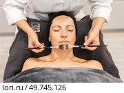 From above crop view of cosmetician applying cleansing oil with brush on face of woman lying face up eyes closed, and covered with gray towel during makeup session in beauty salon. Beautician applying cosmetics on client in beauty center. Стоковое фото, агентство Ingram Publishing / Фотобанк Лори