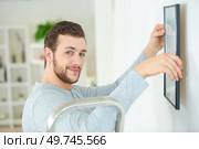 man positioning picture frame on wall. Стоковое фото, агентство Ingram Publishing / Фотобанк Лори