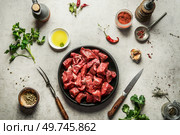 Raw diced beef meat on circle cutting board with fork and knife, herbs and spices for tasty cooking. Goulash food preparation. Top view. Стоковое фото, агентство Ingram Publishing / Фотобанк Лори