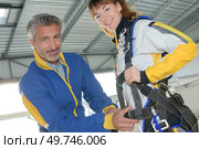 Man attaching harness onto female skydiver. Стоковое фото, агентство Ingram Publishing / Фотобанк Лори