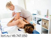 Professional female osteopath in white uniform rubbing back of patient during physiotherapy session in light hospital room. Female physical therapist doing spinal manipulation on patient. Стоковое фото, агентство Ingram Publishing / Фотобанк Лори
