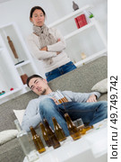 Woman looking disdainfully at young man surrounded by empty beer bottles. Стоковое фото, агентство Ingram Publishing / Фотобанк Лори