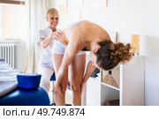 Positive blonde physiotherapist in white uniform rubbing waist of unrecognizable female patient in underwear bending and holding knees during physiotherapy. Female osteopath massaging waist of client during treatment in clinic. Стоковое фото, агентство Ingram Publishing / Фотобанк Лори