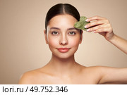 Beauty young woman doing skin care routine, scrapping, massage facial skin with jade gua sha scrapper, Facial treatment for anti aging and cosmetic cleaning. Стоковое фото, агентство Ingram Publishing / Фотобанк Лори