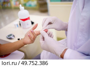 Closeup of standing anonymous pharmacist hands, in medical gloves testing blood of sitting faceless lady customer while diagnosing with tool diabetes and sugar.. Unrecognizable pharmacist in gloves checking blood of anonymous lady customer in pharmacy. Стоковое фото, агентство Ingram Publishing / Фотобанк Лори