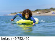 Concentrated young female surfer in wetsuit with curly hair lying on SUP board while paddling with hands floating on ocean during summer vacation. Focused woman on paddleboard rowing with hands in sea. Стоковое фото, агентство Ingram Publishing / Фотобанк Лори