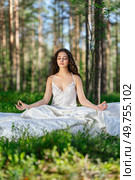 Young woman is resting on a mattress in the lotus position, in summer forest. Girl is sleeping in the woods. Стоковое фото, агентство Ingram Publishing / Фотобанк Лори