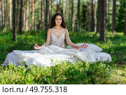 Young woman is resting on a mattress in the lotus position, in summer forest. Girl is sleeping in the woods. Стоковое фото, агентство Ingram Publishing / Фотобанк Лори