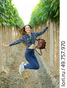 A radiant and cheerful young woman leaps joyfully along a vineyard path, exuding happiness and a sense of freedom while embracing the beauty of nature all around her under the sunny sky. A Joyful Young Woman Jumping Enthusiastically in a Beautiful Vineyard with a Backpack on. Стоковое фото, агентство Ingram Publishing / Фотобанк Лори