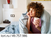 Woman wrapped in blanket enjoying hot beverage and leaning on hand while resting on bed in weekend. Relaxed lady holding cup of hot drink on bed. Стоковое фото, агентство Ingram Publishing / Фотобанк Лори