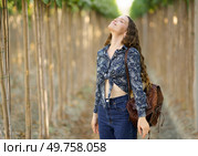 In a sunny vineyard, a young woman stands gracefully among greenery, joyfully embracing nature. Dressed stylishly with a chic brown bag, she radiates tranquility and happiness, a perfect photo moment. A Young Woman Happily Enjoying the Beauty of Nature within a Stunning Vineyard Setting. Стоковое фото, агентство Ingram Publishing / Фотобанк Лори