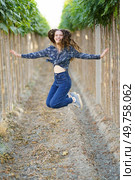 A young woman leaps joyfully in a picturesque vineyard, enveloped by vibrant greenery and blooming vines, perfectly embodying freedom, sheer happiness, and a carefree spirit in nature. Experience the Joyful Jump in the Vineyard A Celebration of Nature and True Freedom. Стоковое фото, агентство Ingram Publishing / Фотобанк Лори