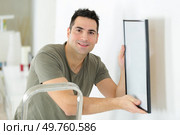 man hanging blank picture on wall. Стоковое фото, агентство Ingram Publishing / Фотобанк Лори