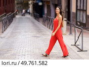 A stylish woman dressed in a vibrant red jumpsuit is elegantly strolling through a picturesque urban alleyway, exuding a remarkable aura of confidence and grace as she enjoys her surroundings. An Elegant Woman Dressed in a Striking Red Suit Walking Gracefully on an Urban Street. Стоковое фото, агентство Ingram Publishing / Фотобанк Лори